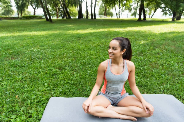 Allegra giovane donna seduta in posa di loto sul tappetino yoga nel parco — Foto stock