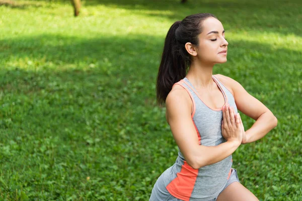 Молода жінка з закритими очима і молитовними руками практикує йогу в парку — стокове фото