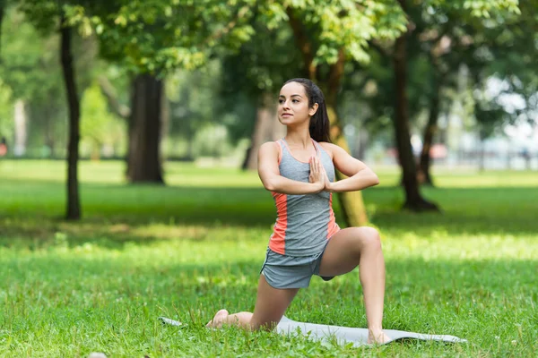 Femme en forme faisant basse pose de fente avec les mains priantes sur le tapis de yoga dans le parc — Photo de stock