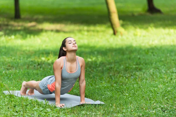 Женщина с закрытыми глазами, растянувшаяся на коврике для йоги в парке — стоковое фото