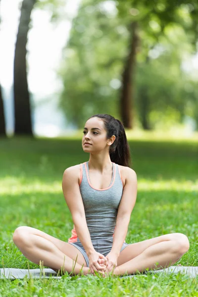 Donna flessibile in abbigliamento sportivo seduta in posa di loto sul tappetino yoga nel parco — Foto stock