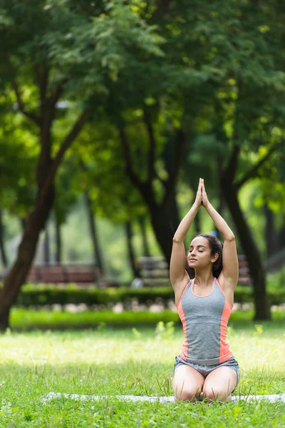 Young woman sitting with praying hands above head while practicing on yoga mat — Stock Photo