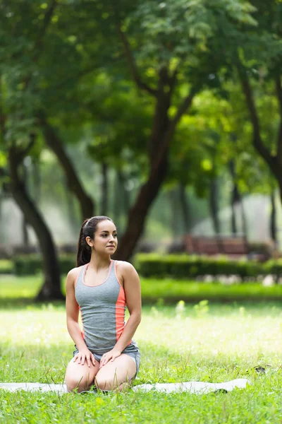 Jovem mulher em forma sentada no tapete toga no parque — Fotografia de Stock