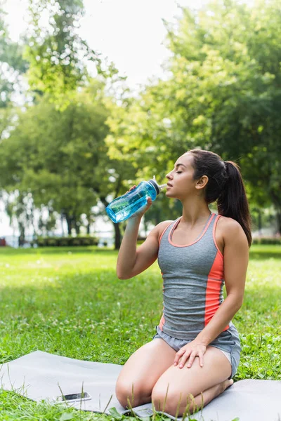 Giovane donna in forma che tiene bottiglia sportiva e acqua potabile nel parco — Foto stock