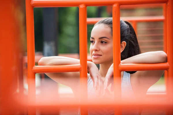 Усміхнена спортсменка дивиться далеко біля оранжевих вертикальних сходів зовні — стокове фото