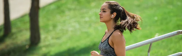 Sportive woman in wireless earphones listening music while running in park — Stock Photo