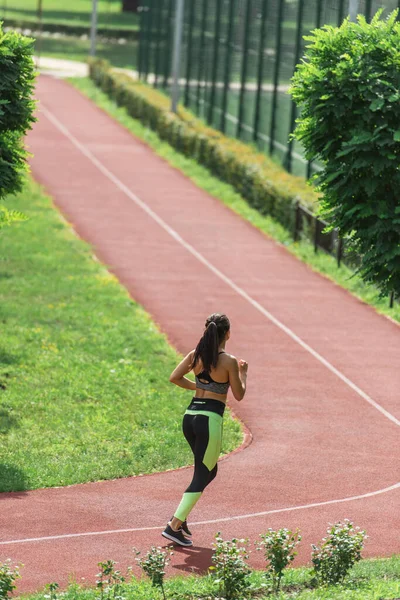 Longitud completa de la mujer deportiva en la parte superior de la cosecha y leggings corriendo en el estadio - foto de stock