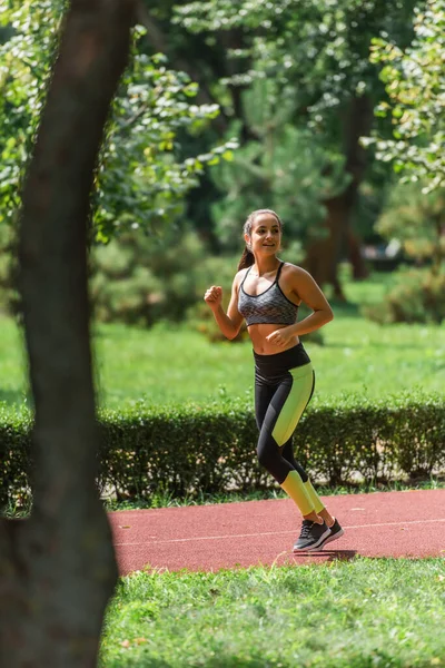 Junge Sportlerin mit drahtlosen Kopfhörern läuft auf Pfad im grünen Park — Stockfoto