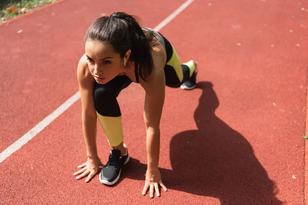 Vue grand angle de la sportive dans les écouteurs sans fil debout dans la pose de départ sur le stade — Photo de stock