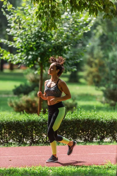 Full length of young athletic woman in wireless earphones running on path in green park — Stock Photo