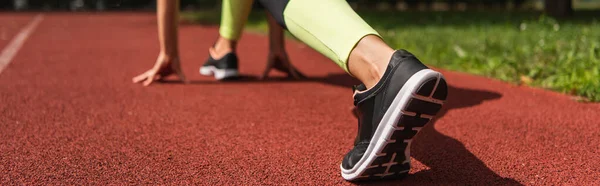 Cropped view of sportswoman in starting pose on stadium, banner — Stock Photo