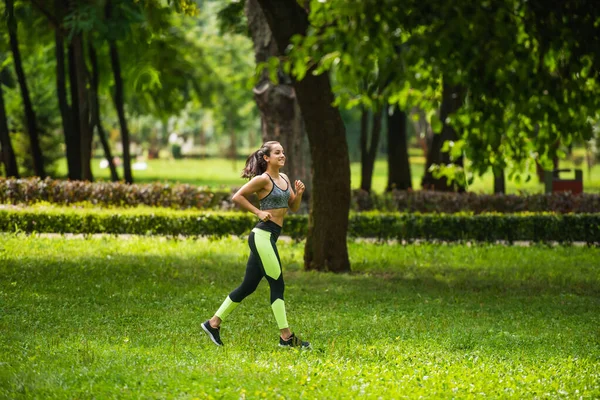 Повна довжина щасливої спортсменки у верхній частині врожаю і легінси бігають на траві в парку — стокове фото