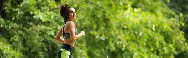 Joven deportista feliz en la parte superior de la cosecha y leggings trotar fuera, bandera - foto de stock