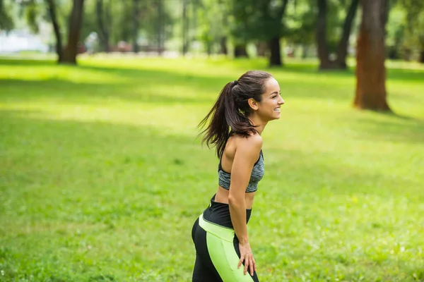Вид збоку щаслива атлетична жінка у верхній частині культури відпочиває, стоячи в зеленому парку — стокове фото