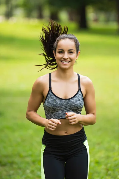 Pleased young woman in crop top and leggings jogging in park — Stock Photo