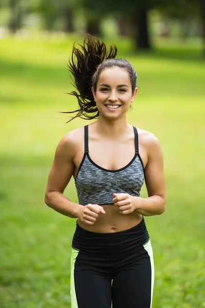 Mujer joven complacida en la parte superior de la cosecha y polainas corriendo en el parque - foto de stock