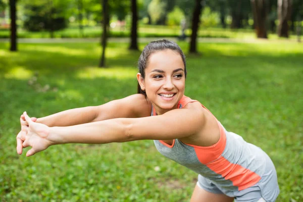 Mujer alegre y deportiva estirándose mientras se calienta en el parque - foto de stock