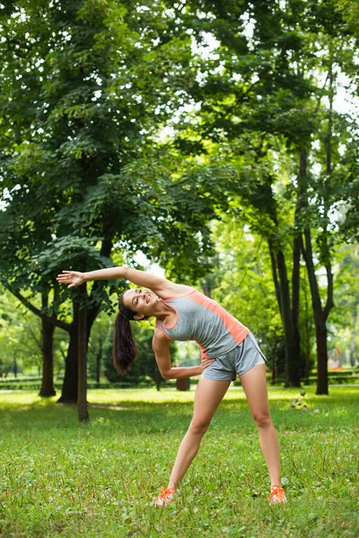 Piena lunghezza di donna gioiosa e sportiva che si esercita con mano sull'anca mentre si riscalda nel parco — Foto stock