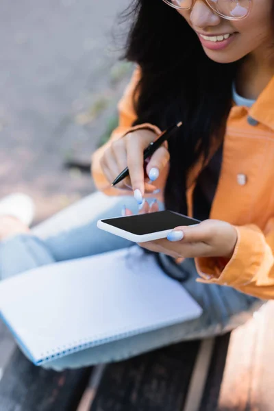 Vista parcial de la mujer sonriente usando el teléfono móvil con la pantalla en blanco al aire libre - foto de stock