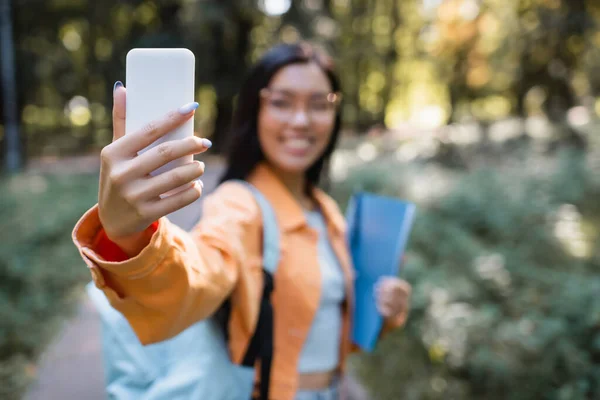 Blurred asian woman taking selfie on mobile phone in park — Stock Photo
