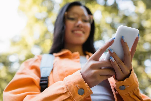 Low angle view of blurred asian woman using mobile phone outdoors — Stock Photo