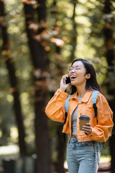 Asian student laughing with closed eyes while talking on smartphone outdoors — Stock Photo