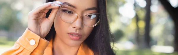 Reflexivo asiático mujer ajustando gafas al aire libre, bandera - foto de stock