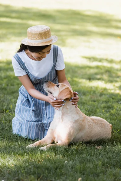 Happy asian woman and yellow labrador looking at each other on grass in park — Stock Photo