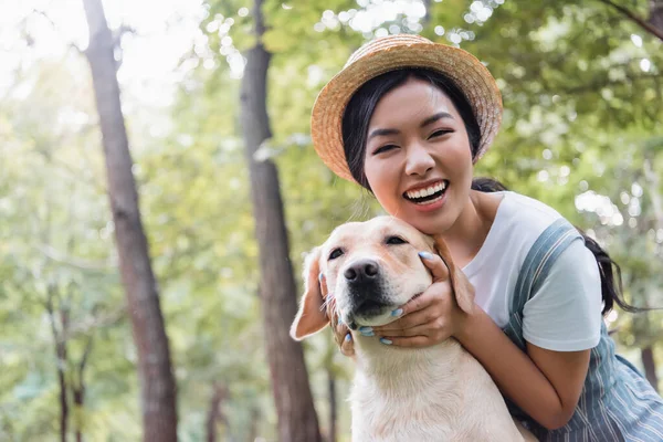 Excited asian woman smiling at camera while hugging dog outdoors — Stock Photo