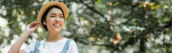 Счастливая женщина в соломенной шляпе, отводящая взгляд на улицу, баннер — стоковое фото