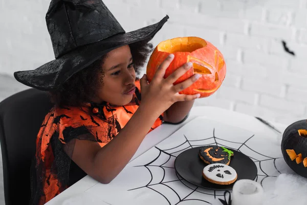 Happy african american girl in witch halloween costume holding caved pumpkin — Stock Photo