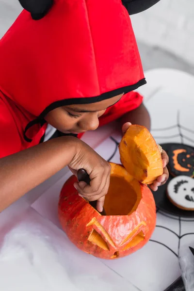 High angle view of african american boy in halloween costume carving pumpkin — Stock Photo