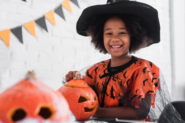 Felice ragazza afro-americana in costume strega di Halloween vicino zucche grotta — Foto stock