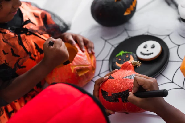 African american boy in halloween costume drawing on pumpkin near sister — Stock Photo