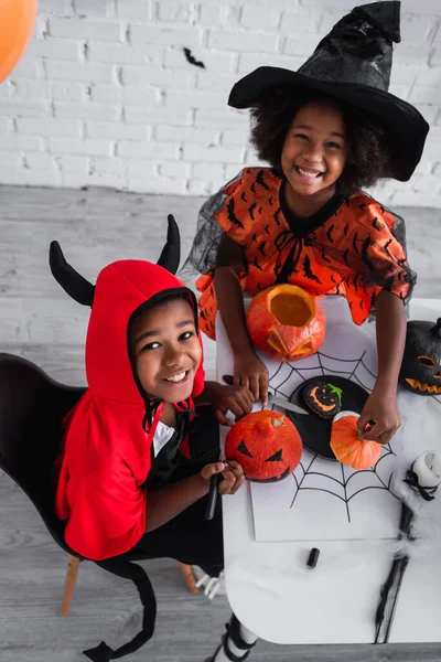 High angle view of happy african american children in halloween costume decorating pumpkins — Stock Photo