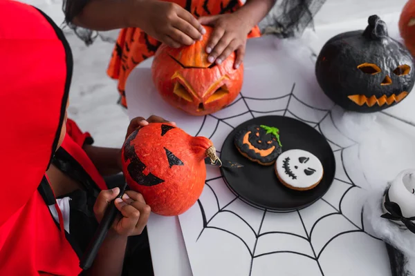 African american kid in halloween costume drawing on pumpkin near sister — Stock Photo