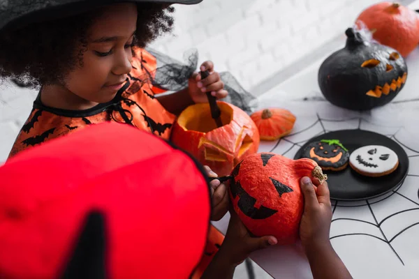 African american girl drawing on pumpkin of blurred brother — Stock Photo