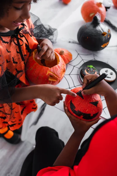 Happy african american girl pointing at drawing on pumpkin near brother — Stock Photo