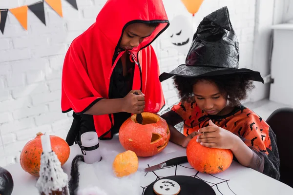 Crianças africanas americanas em trajes de Halloween esculpindo abóboras — Fotografia de Stock