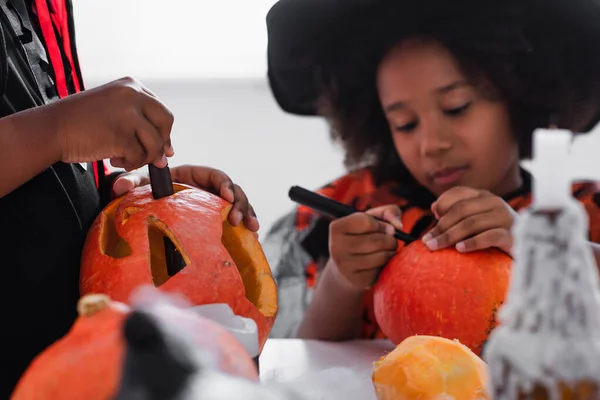 Africano americano ragazzo intaglio zucca mentre sorella disegno su sfondo sfocato — Foto stock