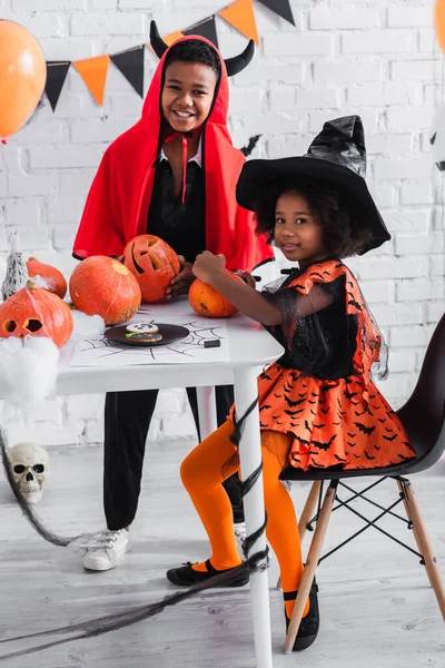 Афроамериканські діти в костюмах Хеллоуїна посміхаються біля різьблених гарбузів — стокове фото