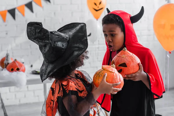 Enfants afro-américains effrayants en costumes d'Halloween tenant des citrouilles sculptées à la maison — Photo de stock