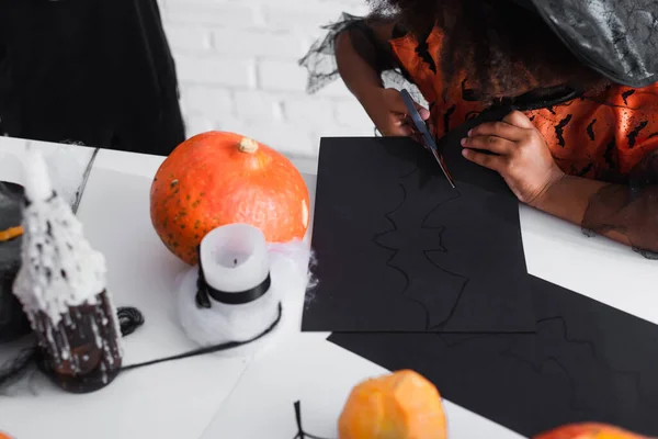 Vue recadrée de l'enfant afro-américain coupant le carton noir avec le modèle de chauve-souris — Photo de stock