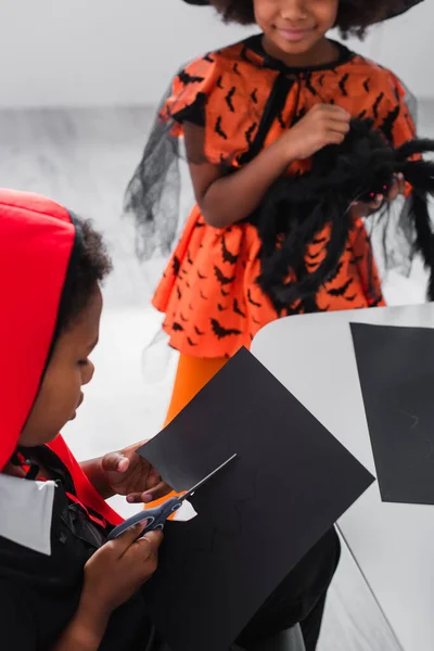 Africano americano bambino taglio nero cartone con modello di pipistrello vicino sorridente sorella — Foto stock