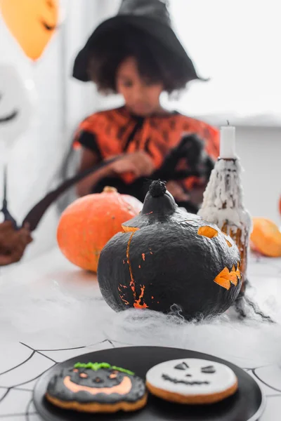 Kekse und geschnitzter Halloween-Kürbis in der Nähe verschwommener afrikanisch-amerikanischer Kinder — Stockfoto