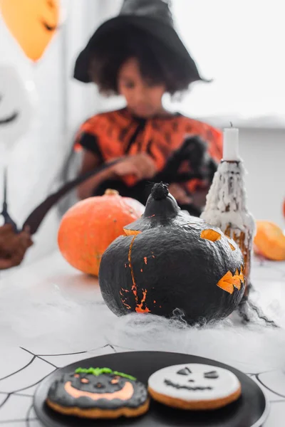 Biscoitos e abóbora halloween esculpida perto de crianças afro-americanas borradas — Fotografia de Stock