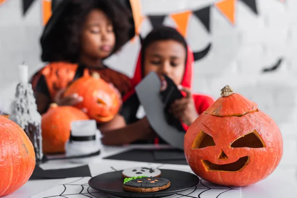 Carved jack o lantern near cookies and blurred african american kids — Stock Photo