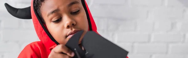 Afrikanisch-amerikanischer Junge im Halloween-Kostüm schneidet Karton mit Schere, Banner — Stockfoto