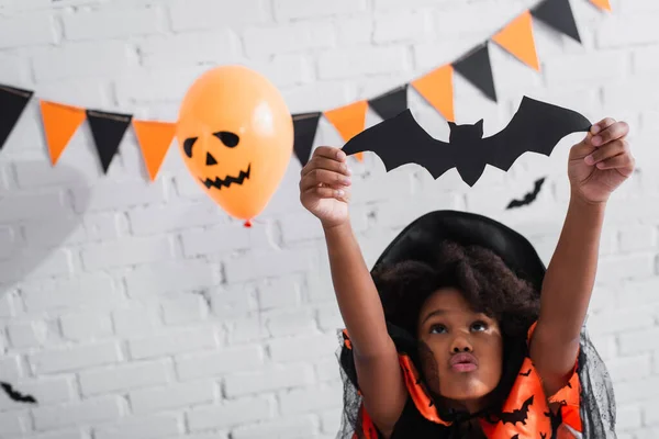 African american girl in halloween costume holding paper cut bat — Stock Photo