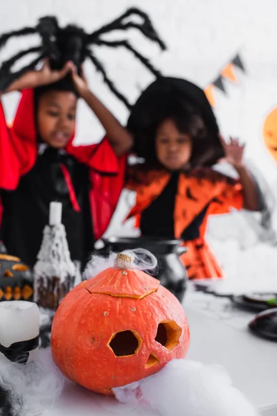 Citrouille sculptée et effrayante près des enfants afro-américains flous en costumes — Photo de stock